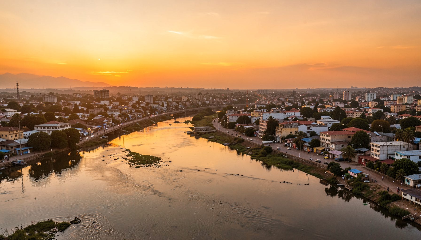 Панорамски поглед на Бамако при зајдисонце, со реката Нигер што тече низ градот, топли златни и портокалови тонови над хоризонтот